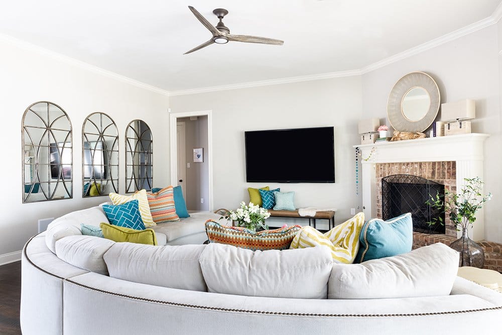 Before and After: A Fresh + Cozy Waco Living Room designed by Lesley Myrick with a custom curved sectional and colorful pillows in teal, chartreuse, and red. 