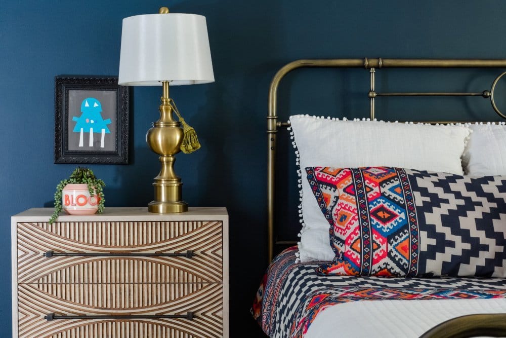 A carved wooden nightstand and colorful bedding in a navy master bedroom by interior designer Lesley Myrick