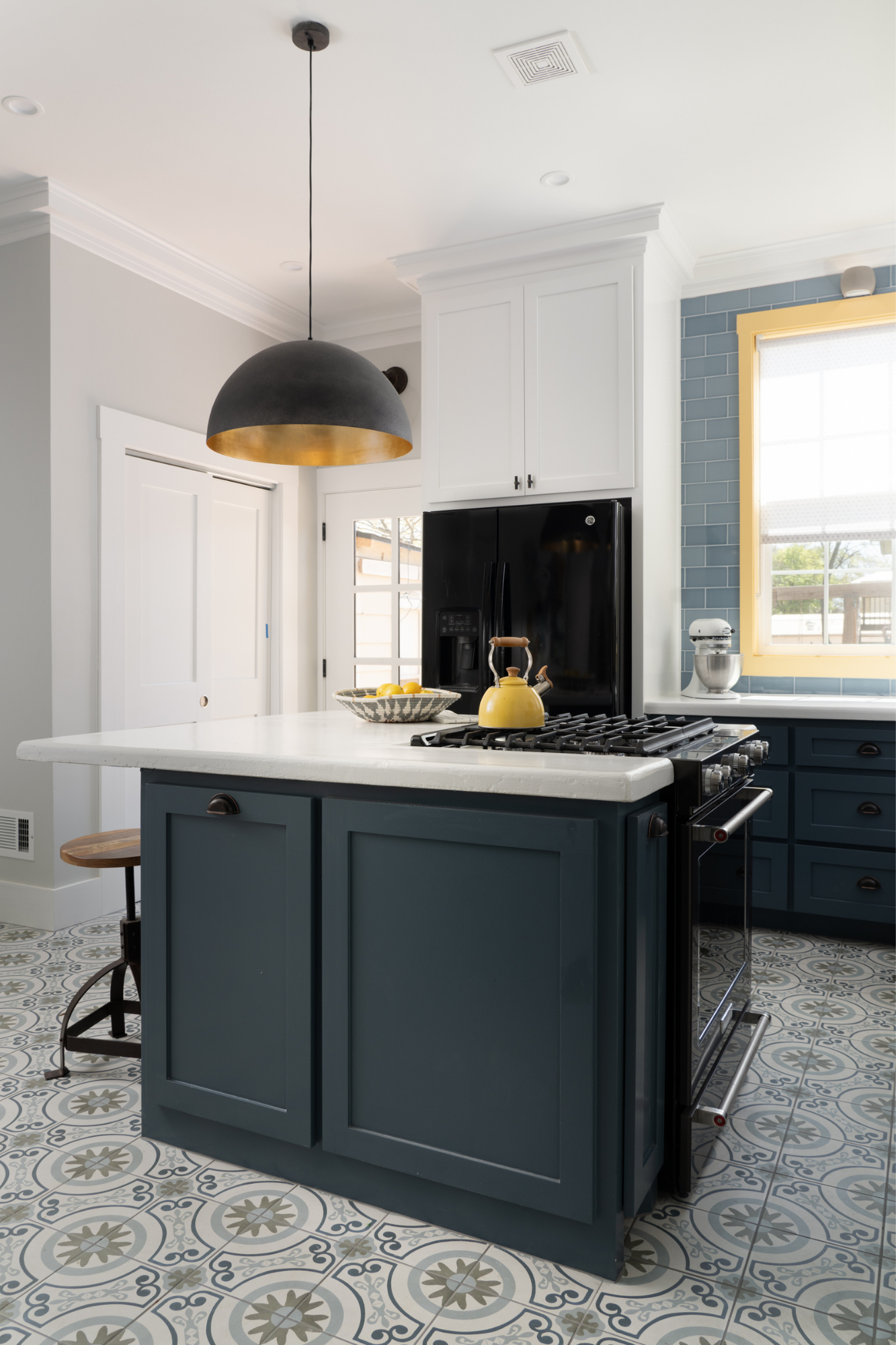 A dramatic oversize black and brass pendant is the centerpiece in this historic blue kitchen remodel by interior designer Lesley Myrick.