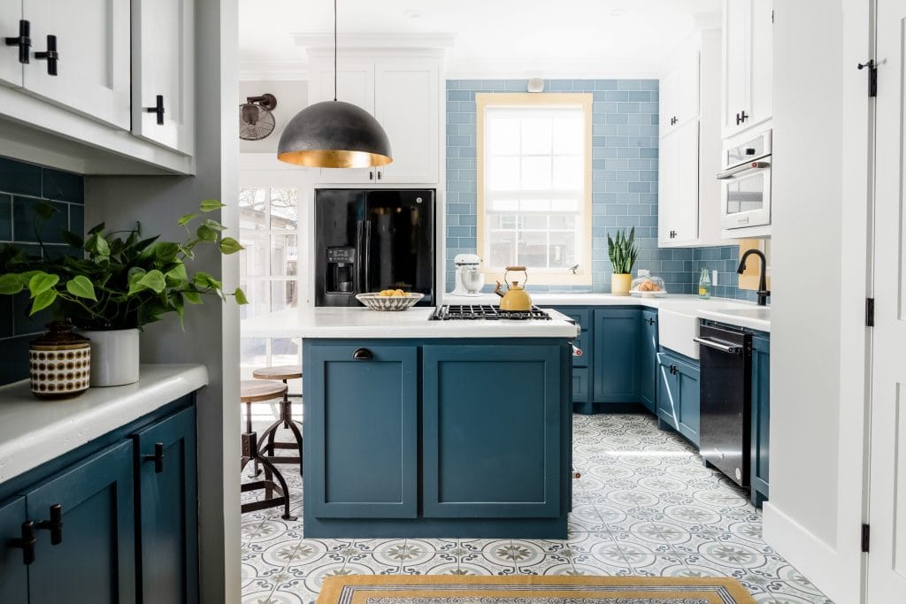 Bright blue and white kitchen with a patterned tile floor, blue subway tile backsplash, brass and black hardware, and a central island with a gas cooktop.