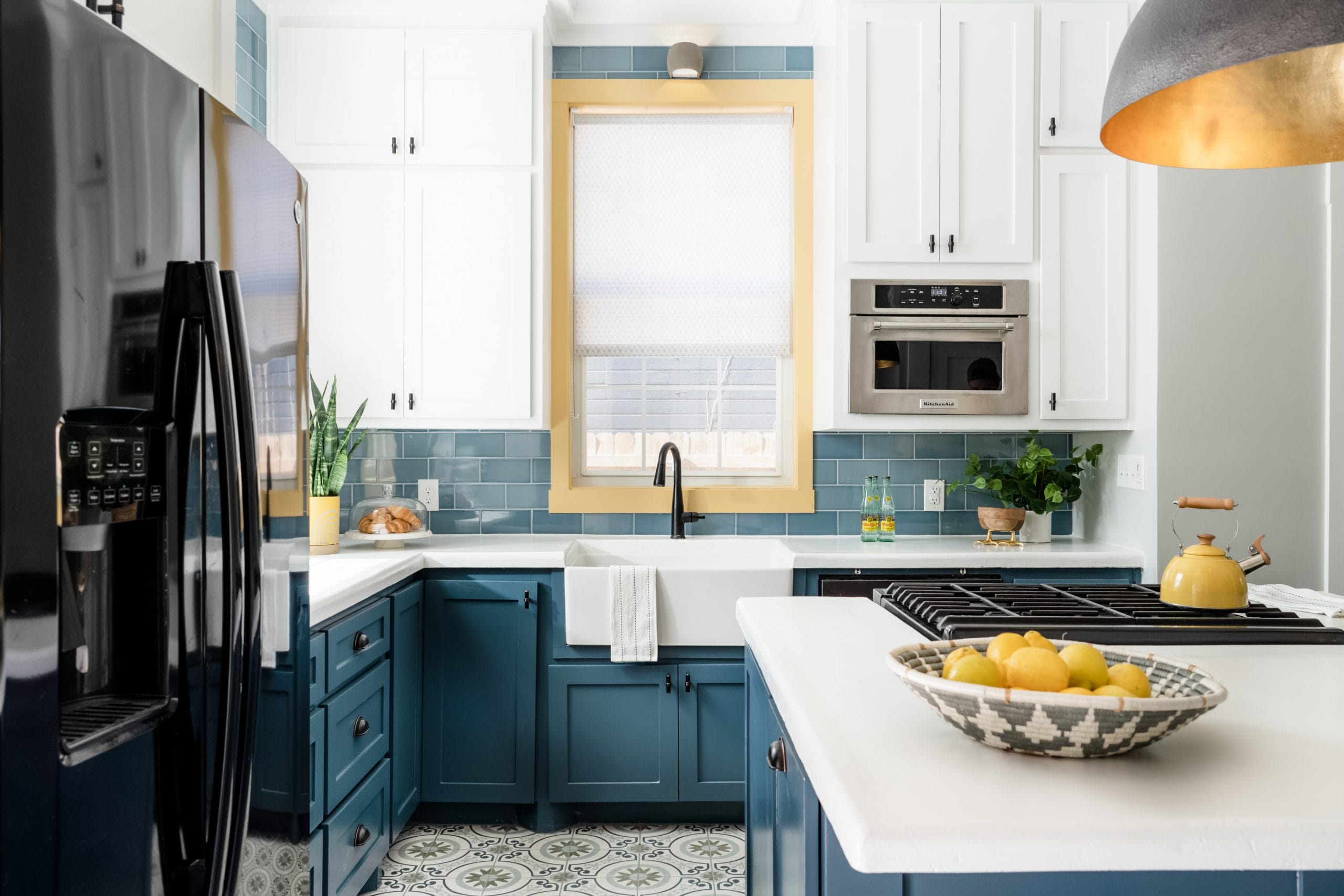 Bright blue and white kitchen with a patterned tile floor, blue subway tile backsplash, brass and black hardware, and a central island with a gas cooktop.