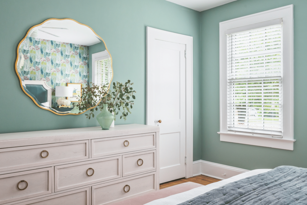 A gold scalloped mirror and whitewashed dresser pop agains sea green walls in this modern Macon bungalow bedroom designer by Atlanta interior designer Lesley Myrick. 