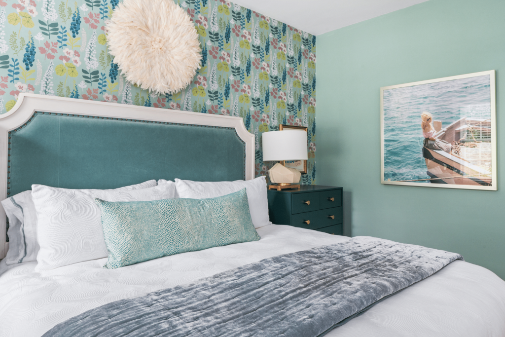 Teal floral wallpaper, a custom teal velvet bed, a vintage Slim Aarons photograps, and a custom lumbar pillow in Kravet fabric in this bedroom by Lesley Myrick Interior Design.
