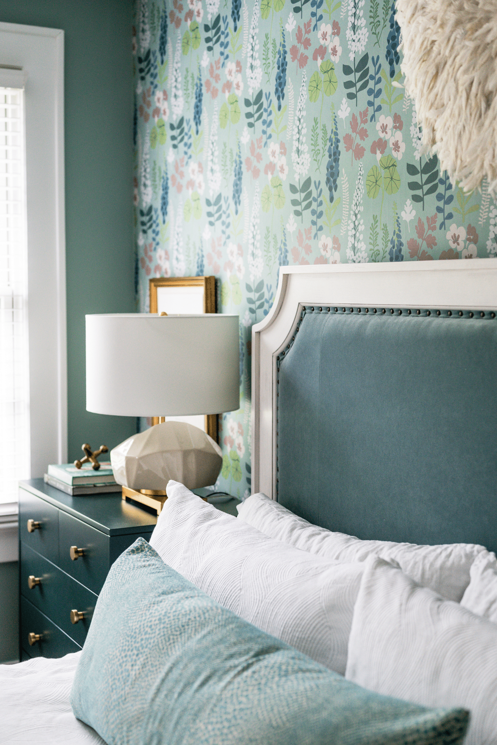 A vignette of a modern Macon bedroom with colorful floral wallpaper, teal bed, and teal nightstands. 