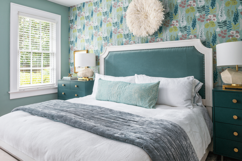 A modern macon bungalow bedroom with colorful floral wallpaper, teal bed, and teal nightstands. 