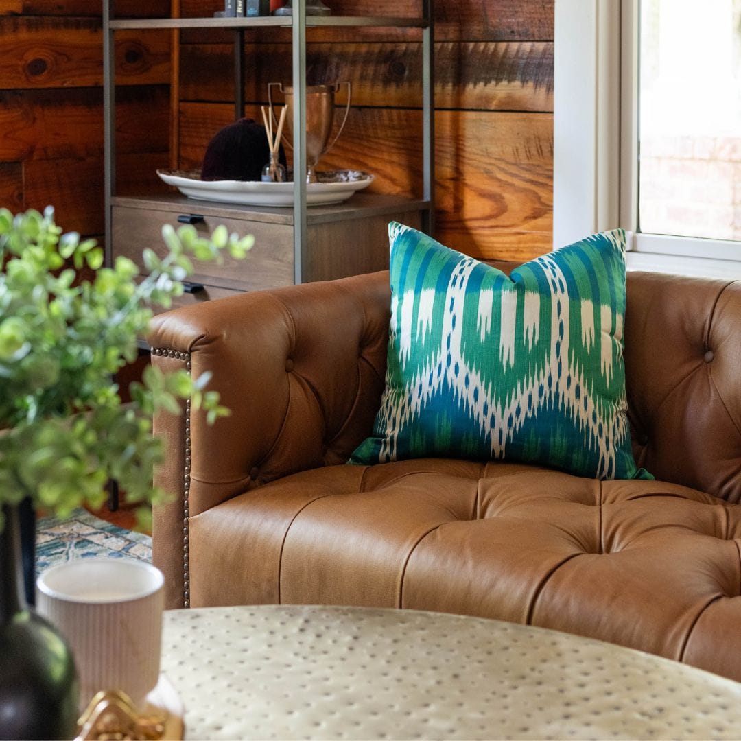 Brown tufted leather sofa with green ikat cushion in a personality-driven lounge design by Lesley Myrick.