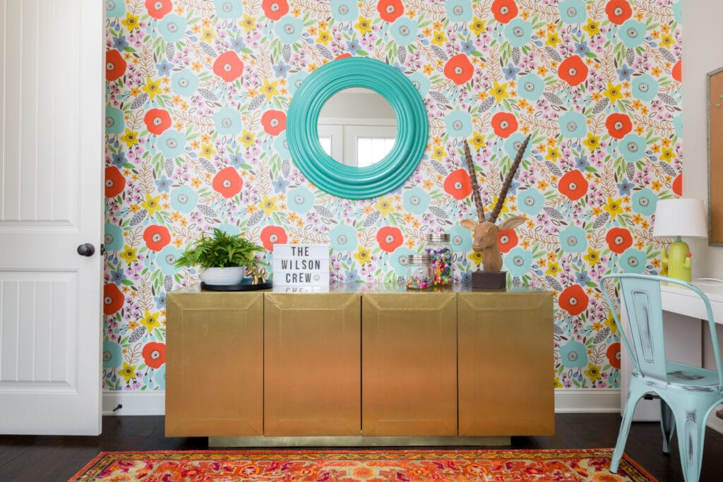 Bright floral wallpaper creates a playful accent wall in a colorful home office with a gold cabinet, turquoise mirror, and vibrant decor. By award-winning Macon interior designer Lesley Myrick.