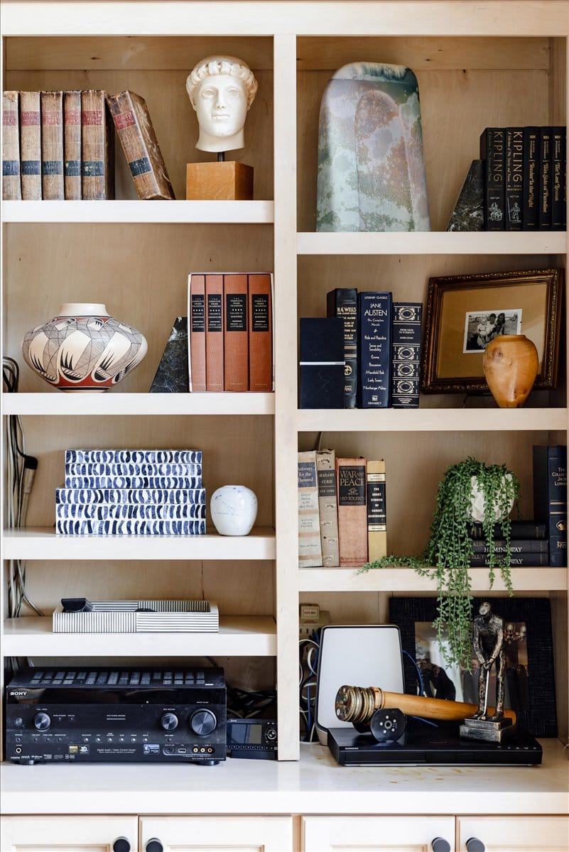 Styled built-in bookshelf with vintage books, decorative vases, framed art, greenery, and eclectic accessories by Lesley Myrick Interior Design.