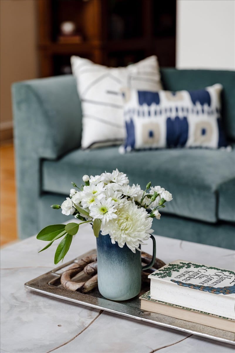 Close-up of coffee table styling with florals and books in front of a teal velvet sofa.