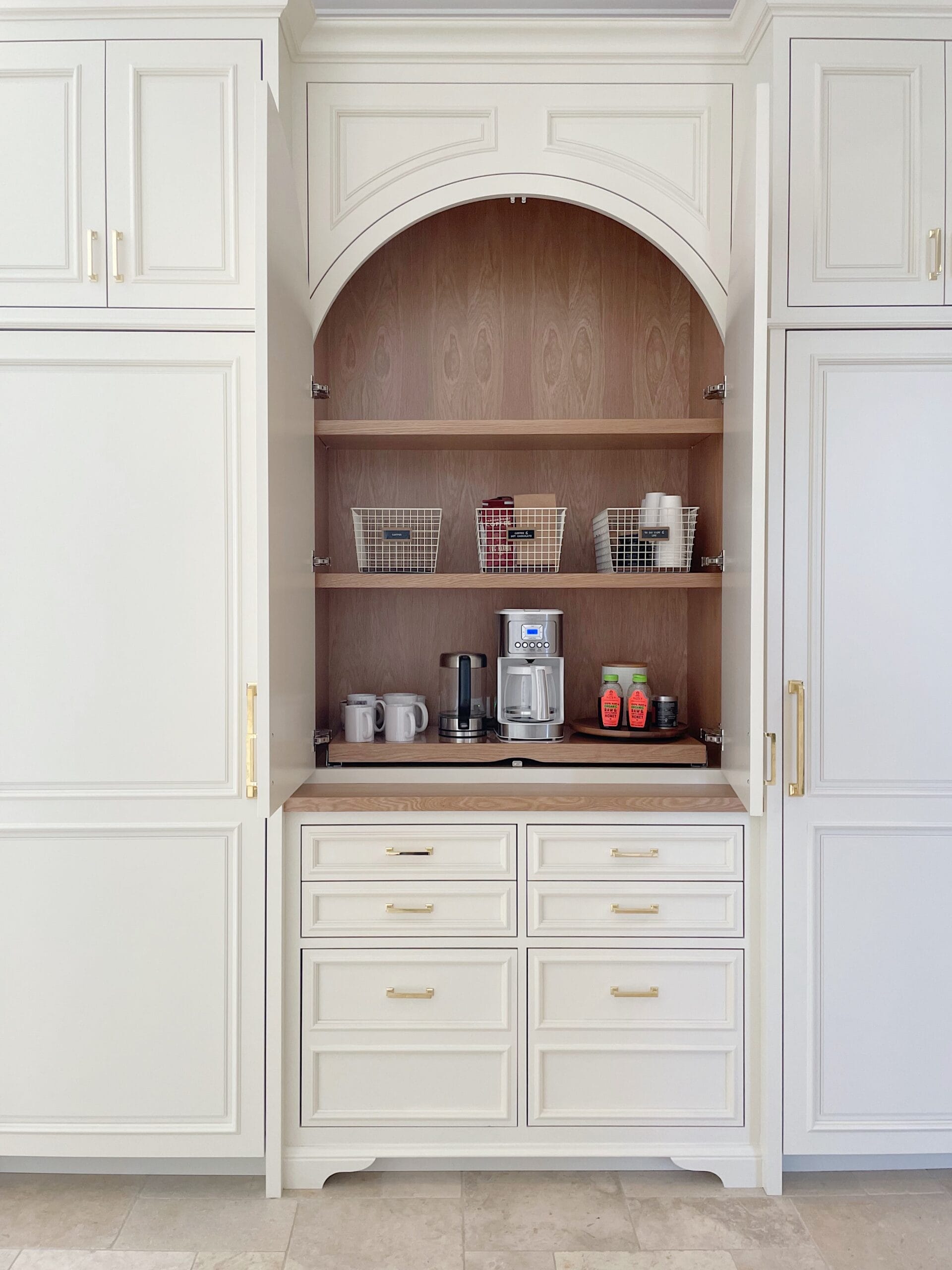 Built-in coffee station with white cabinetry, open wood shelving, and organized baskets for mugs and supplies.