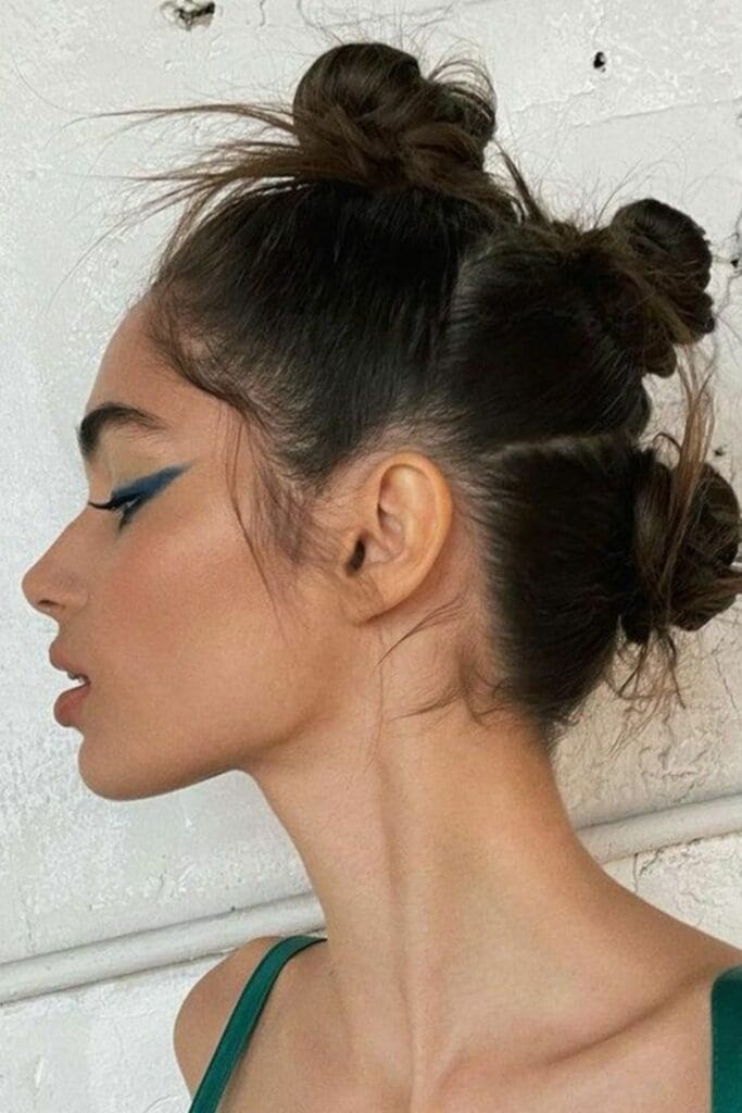 A model with teal winged eyeliner and multiple hair buns