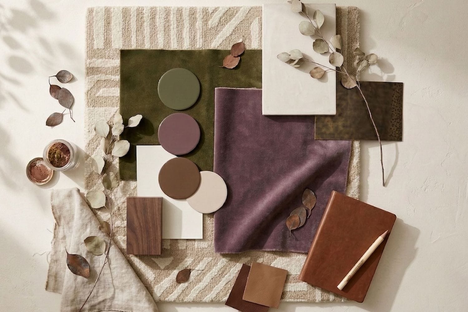 A materials palette with plum, olive green, cognac, natural linen, and textured modern neutral carpet.