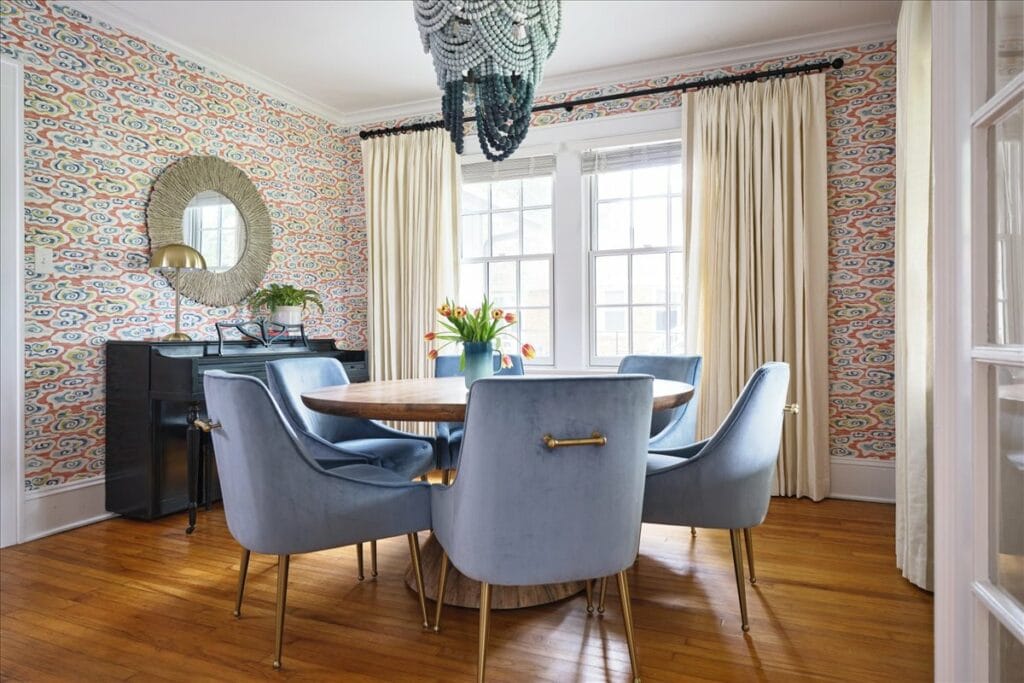 A dining room with bold blue and orange wallpaper and a blue beaded chandelier designed by Lesley Myrick.